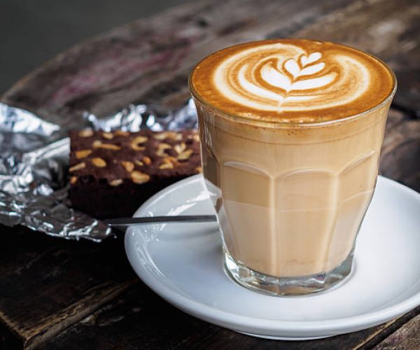 A cup of hot latte art or cappuccino coffee on old wooden table with brownie cake on foil