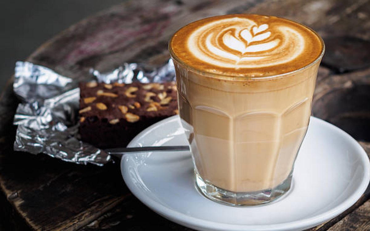 A cup of hot latte art or cappuccino coffee on old wooden table with brownie cake on foil